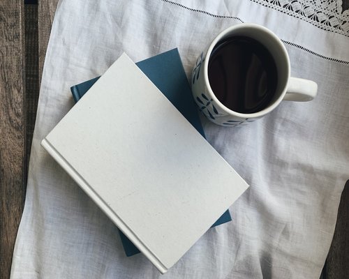 A cup of tea next to a book on a wooden table